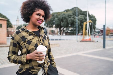 Portrait of beautiful afro american latin woman holding a cup of coffee outdoors in the street....