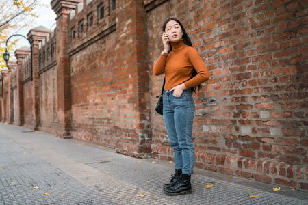 Portrait of young Asian woman talking on the phone outdoors in the street. Urban and communication concept.の写真素材