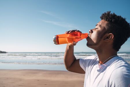 Portrait of an athletic man drinking something after training at the beach. Sport and health...