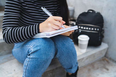 Portrait of a woman, writing on notebook while sitting outdoors on concrete stairs.の写真素材