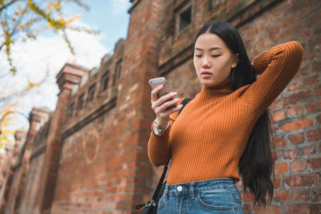 Portrait of young Asian woman using her mobile phone outdoors in the street. Urban and communication concept.の写真素材