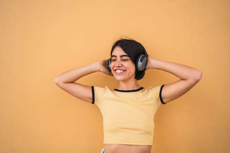 Portrait of young latin woman listening to music with headphones against yellow background. Urban concept.の写真素材