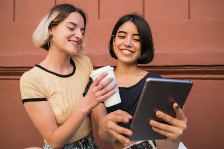 Portrait of lovely lesbian couple spending time together and taking selfie with digital tablet outdoors at the street. LGBT concept.の写真素材