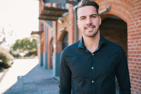 Portrait of attractive young man wearing casual clothes, standing outdoors with urban background.
