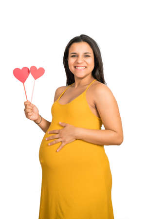 Close-up of pregnant woman holding heart sign against white background. Pregnancy, motherhood concept.の写真素材