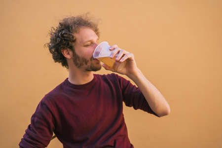 Portrait of young man enjoying and drinking beer against yellow background. Lifestyle concept.