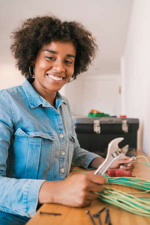 Portrait of young afro woman fixing electricity problem with cables at new home. Repair and...