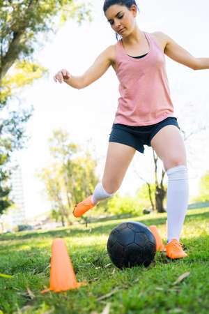 Portrait of young female soccer player running around cones while practicing with ball on field. Sports concept.の写真素材