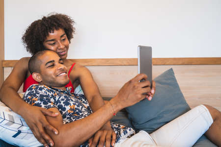 Portrait of young latin couple taking a selfie with digital tablet at home. Technology and lifestyle...
