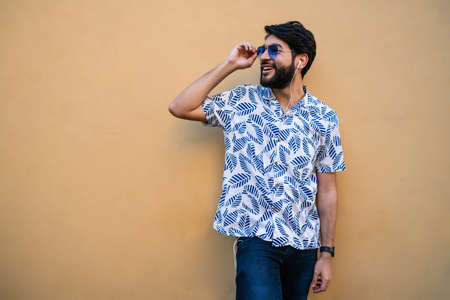 Portrait of young latin man wearing summer clothes and listening to music with earphones against...