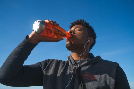 Portrait of an athletic man drinking something after training at the beach. Sport and health lifestyle.の写真素材
