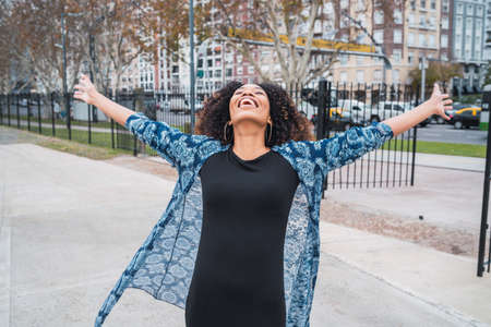 Portrait of young afro american woman standing outdoors with arms raised and laughing.の写真素材