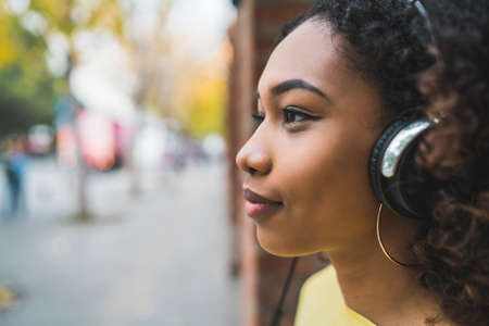 Portrait of young Afro american woman listening to music with headphones in the street. Outdoors.