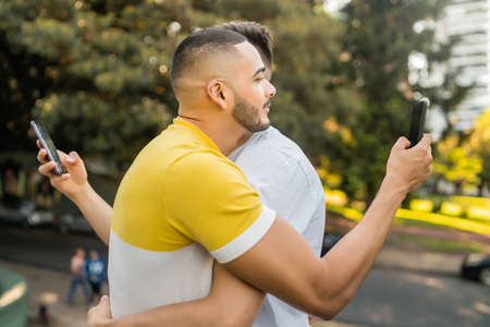Portrait of young gay couple hugging while each using their smartphone. Couple problem and Lgbt concept.の写真素材
