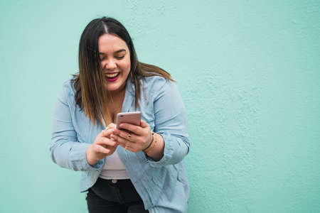 Portrait of young plus size woman smiling while typing text message on her mobile phone outdoors....