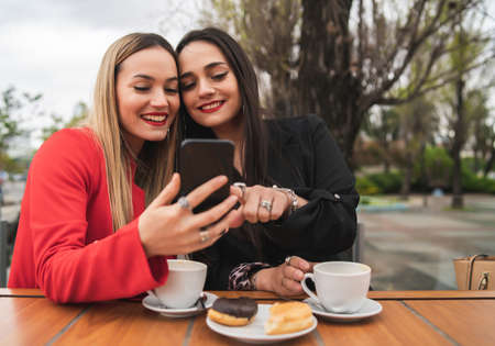 Portrait of two young friends using their mobile phone while sitting at coffee shop. Lifestyle and friendship concept.の写真素材