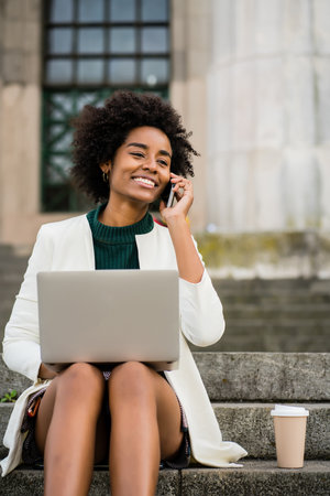 Business woman talking on phone and using laptop outdoors.の写真素材