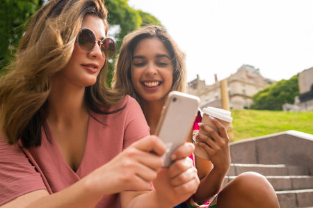 Two friends using mobile phone outdoors.の写真素材
