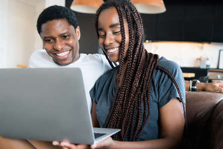 Couple using laptop while sitting on couch at home.