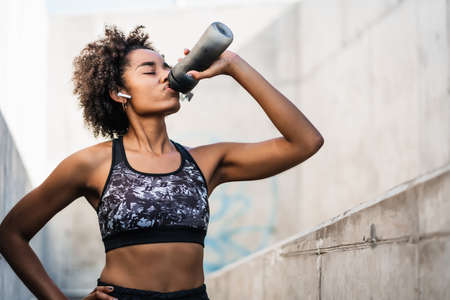Afro athlete woman drinking water after work out outdoors.の写真素材