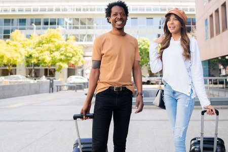 Tourist couple carrying suitcase while walking outdoors.の写真素材