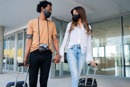 Tourist couple carrying suitcase while walking outdoors.の写真素材