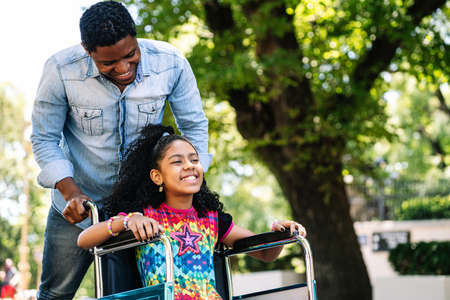 Little girl in a wheelchair enjoying a walk with her father.の写真素材