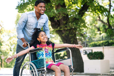 Little girl in a wheelchair enjoying a walk with her father.の写真素材