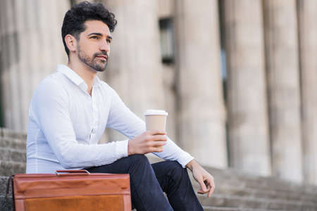 Portrait of business drinking coffee on stairs outdoors.の写真素材