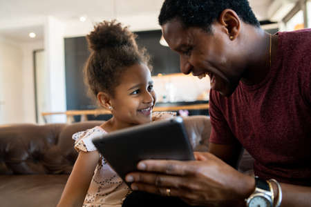 Father and daughter using digital tablet at home.