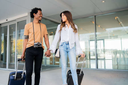 Tourist couple carrying suitcase while walking outdoors.