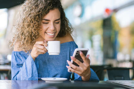 Latin woman using a mobile phone at a coffee shop.の写真素材