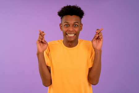Afro young man crossing her fingers wishing good luck.