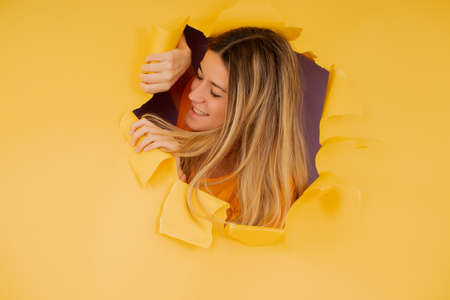 Young woman looking through a torn hole in paper wall.