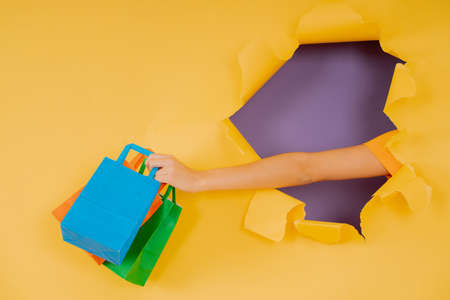 Hand holding shopping bags through a hole in paper wall.の写真素材