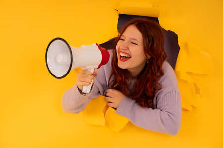 Woman using a megaphone through a hole in a paper wall.の写真素材