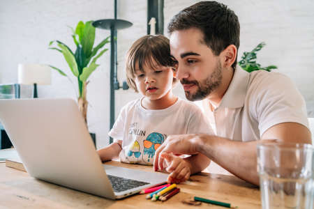 Little boy and his father using a laptop at home.の写真素材