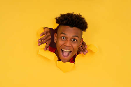 Afro man looking through a torn hole in paper wall.の写真素材