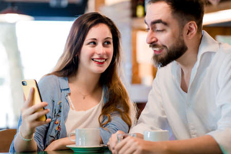Two people using a mobile phone together at a coffee shop.