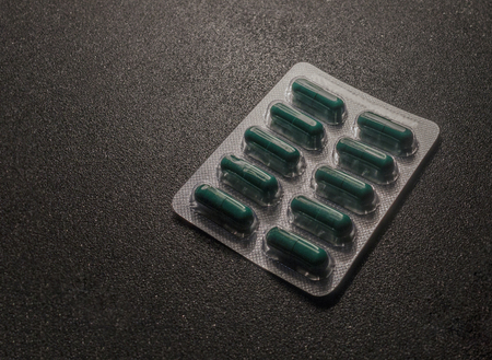 Green pills in blister pack on the plastic surface.Plate of tablets on the black desk. Blister with green pillsの写真素材