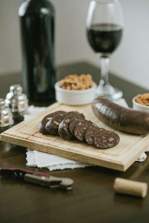 Sliced blood sausage on wooden board with peanuts and red wine