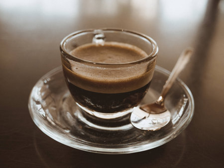 Glass coffee cup, dark espresso with foam and spoon, isolated, old filterの写真素材