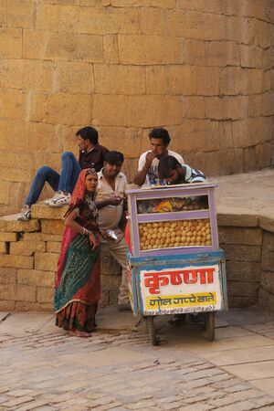 Jaisalmer Rajasthan, India, 2017, march 24: woman in Sari and four men eating street food pani puri from a vehicle stand in the desert town Jaisalmer in front of the fortのeditorial素材