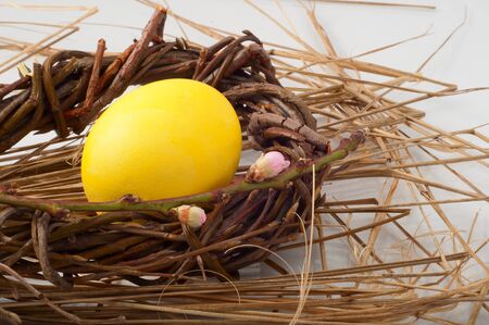 yellow Easter egg in a wicker wreath and with a branch of a blossoming peachの写真素材
