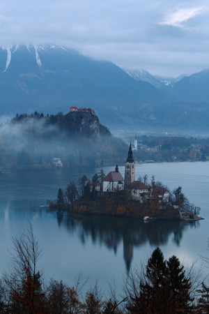 Bled Island on Lake Bled, Slovenia on a cloudy day with castle behind and snowy mountains.のeditorial素材