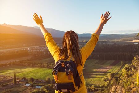Young woman stands at the top of a hill with her arms raised at golden hourの写真素材