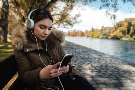 A pretty caucasian woman using her smartphone and listening music beside a lake at park. Copy spaceの写真素材