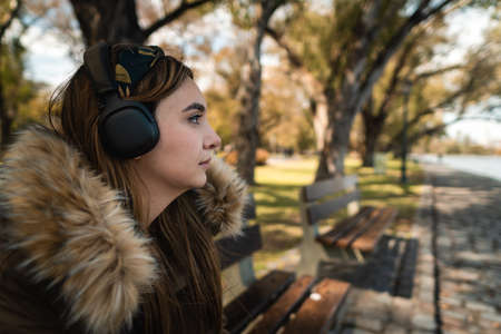A pretty caucasian woman listening music at park and looking at side. Copy spaceの写真素材