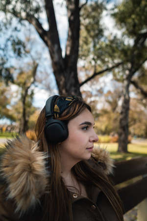 Profile shot of a pretty caucasian woman listening music at park and looking at side. Verticalの写真素材
