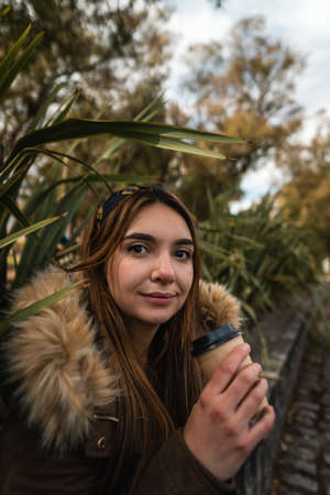 A pretty woman smiling at camera while relaxing at park and drinking a coffee. Verticalの写真素材